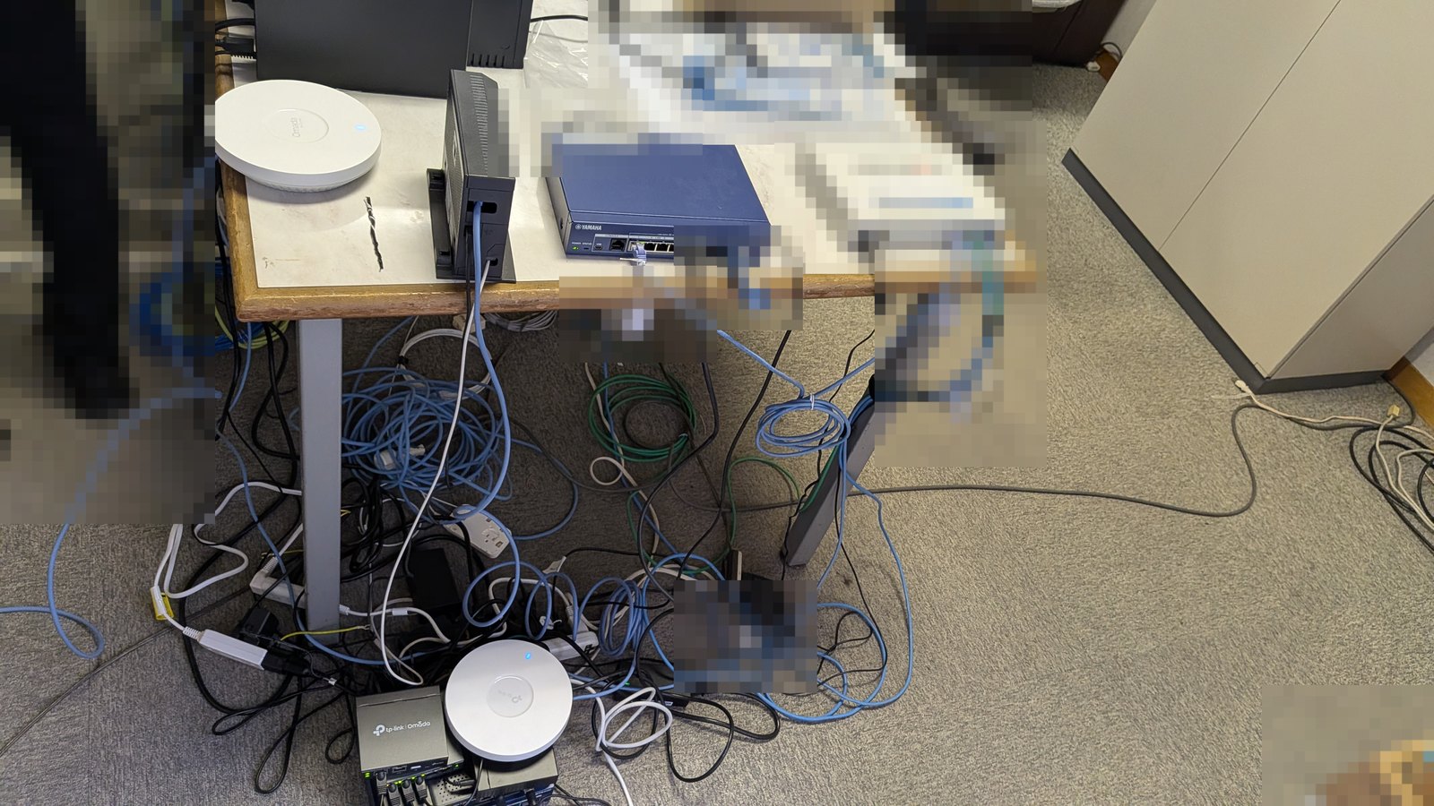 机の上と床に露出して置かれていたルーターやスイッチ、無線アクセスポイントと配線